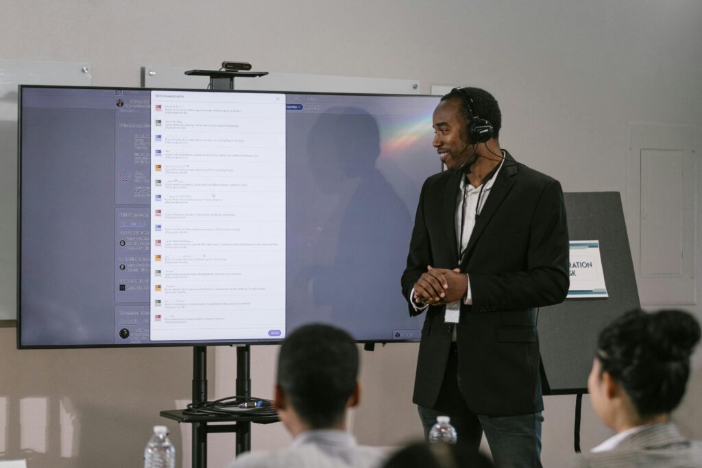 pexels-photo-7648507-7648507 An adult man presents at a technology seminar using a large screen and headset.